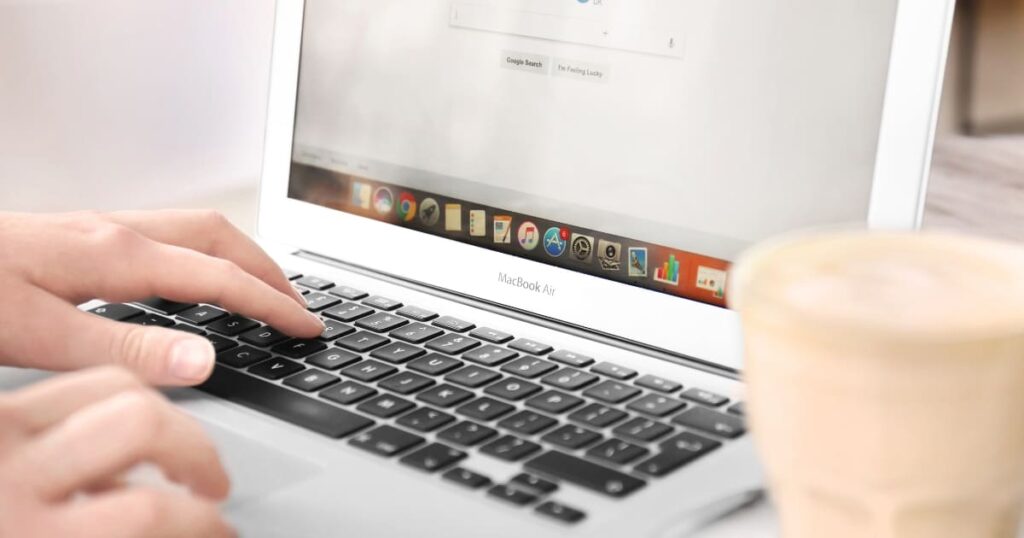 Persona usando laptop para buscar información de negocios en Google, con una taza de café al fondo.